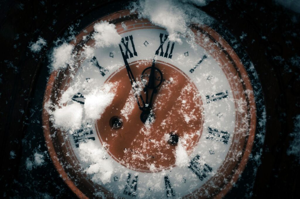 Close-up of a snow-covered Roman numeral clock indicating winter season and time passage.