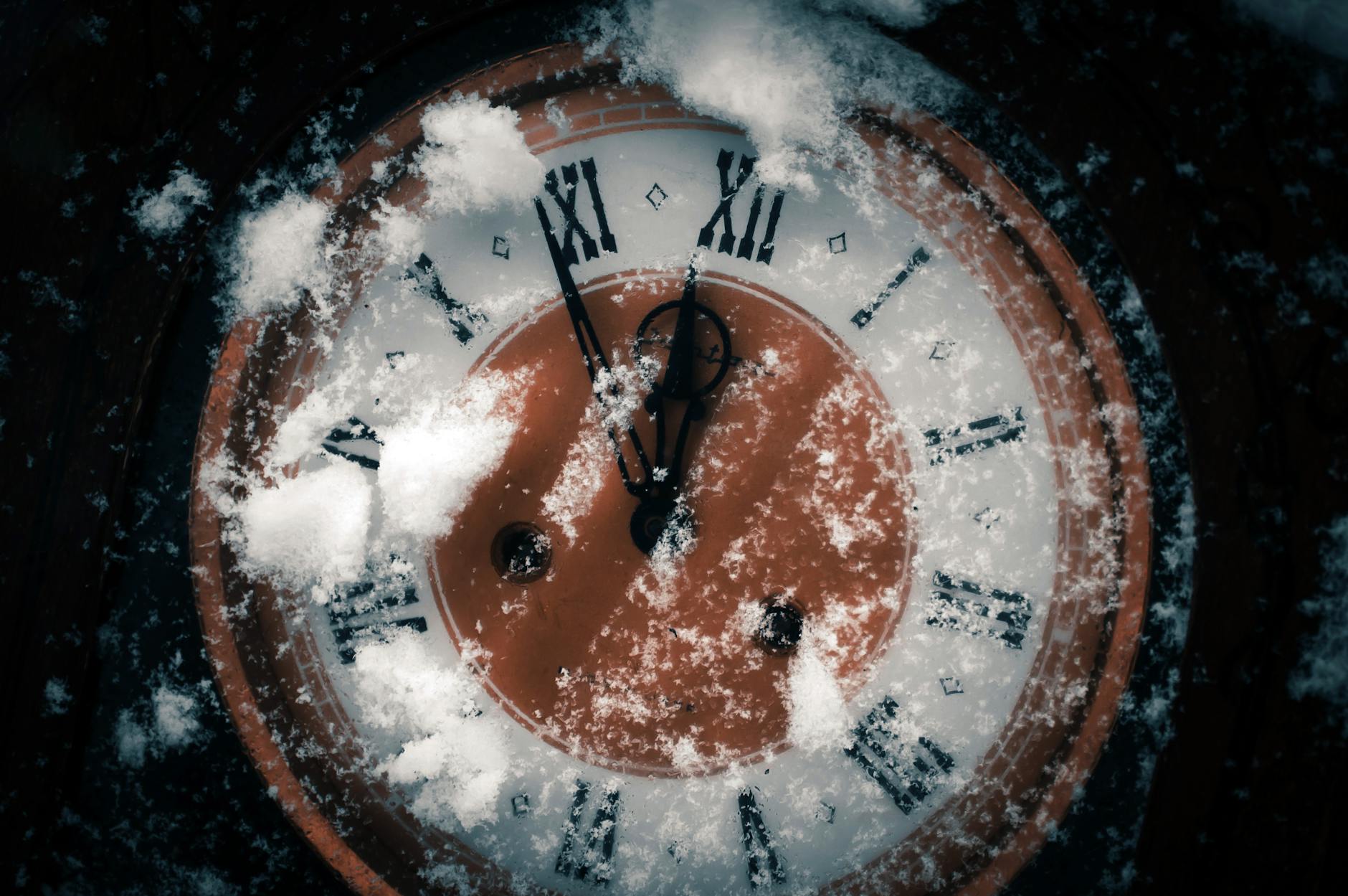 Close-up of a snow-covered Roman numeral clock indicating winter season and time passage.